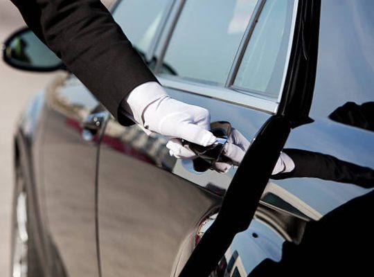 The white gloved hand of a uniformed chauffeur / doorman opening / closing a luxury car door.